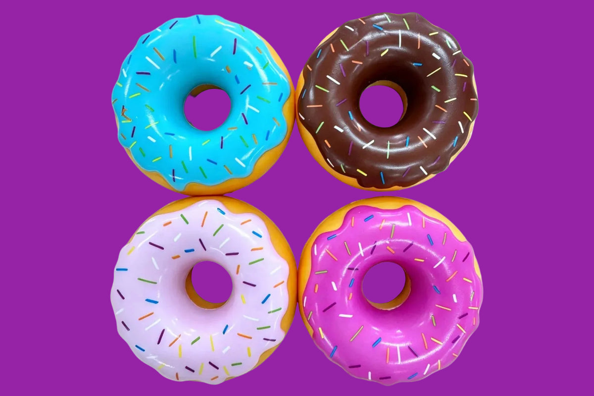 Four donuts arranged in a 2x2 grid on a white background, each with different frosting colors and sprinkles: blue, brown, light purple, and pink.